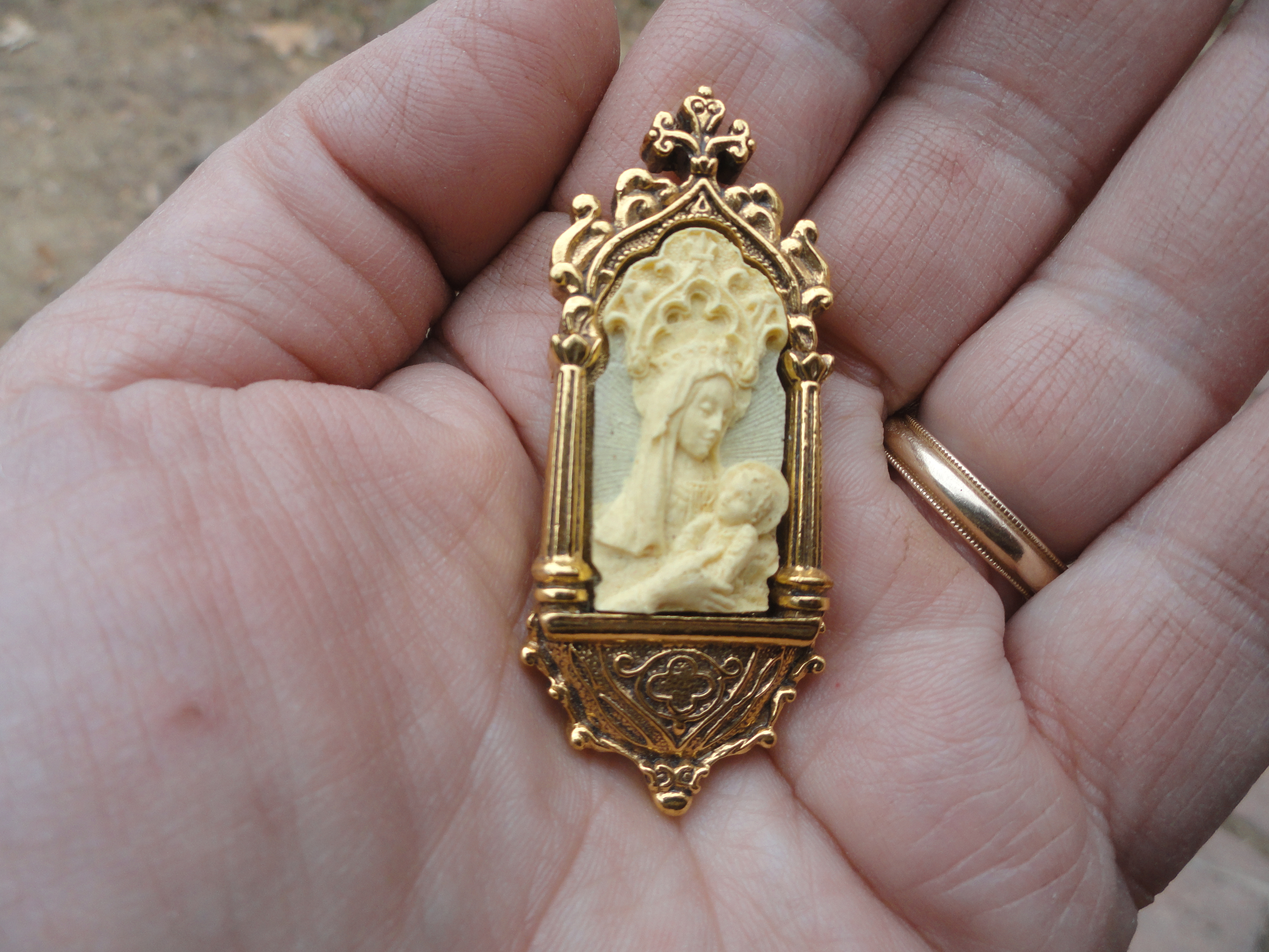 reproduction of Madonna and Child in an ornate metal frame, in the palm of a hand