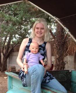 teen Holly sitting up on the side of a pickup bed, with a baby doll