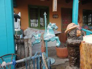 smallish  carousel horse, wooden statue of Smokey Bear, an iron wheel, other stuff, outside an antique shop in Capitan, New Mexico