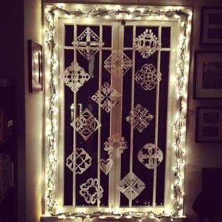  dark window with white fairy lights around the frame and paper snowlflakes fastened up