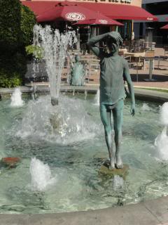 cast statue of a young person, eyes shaded by hand, standing in the pool of a fountain