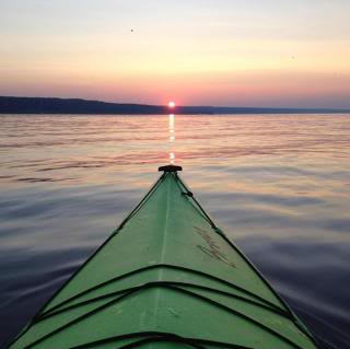 front of a kayak, pointing at the setting sun